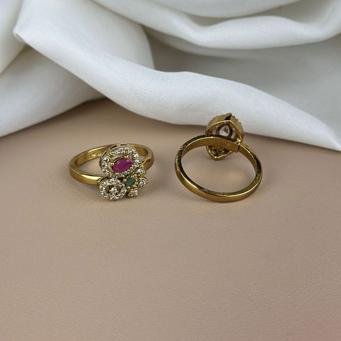 Gold ring with gemstones and gold hoop earring on a beige surface with white fabric