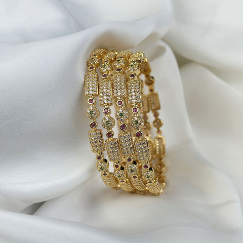 Set of gold bangles with gemstones on a white fabric background