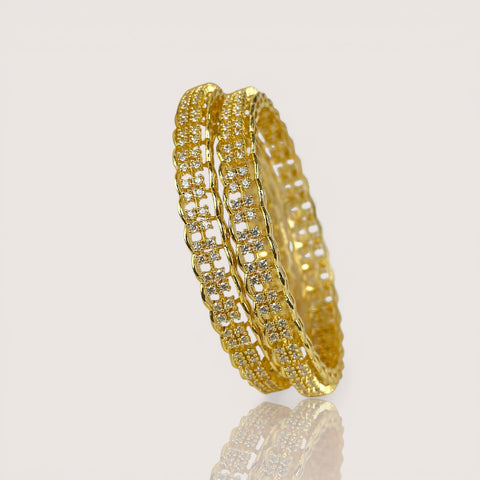Gold bangles with embedded stones on a light gray background