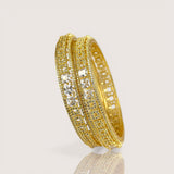 Gold bangles with embedded stones on a light gray background