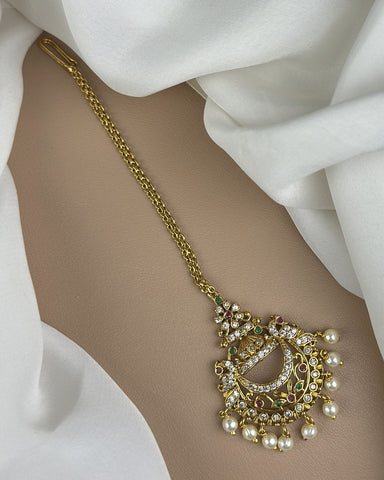 Gold anklet with intricate design on a white fabric background