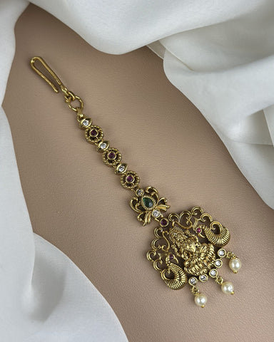 Gold bracelet with intricate design and gemstones on a white fabric background