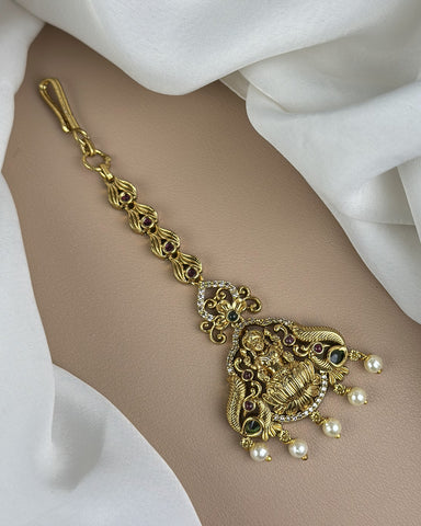 Gold bracelet with intricate design and pearl accents on a white fabric background