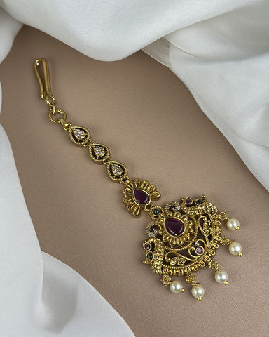 Ornate gold bracelet with gemstones and pearls on a white fabric background