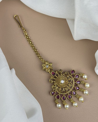 Decorative gold necklace with purple stones and pearl-like beads on a neutral background
