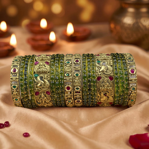A stack of ornate Indian bangles (batches) featuring green stone inlays and gold-plated metal with detailed motifs, displayed on a beige satin fabric with blurred diya candles in the background.
