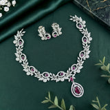 Silver-toned jewelry set featuring a necklace and matching earrings with intricate leaf motifs and deep pink gemstone accents, arranged on a dark green satin fabric background.