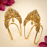 A pair of ornate gold-toned traditional Indian hair ornaments (Jhumkas) with detailed filigree, small hanging gold beads, and tiny colored gem accents, displayed on a light cream background with decorative pink flower petals in the corners.