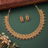 Gold-toned traditional necklace and matching earrings with small pink gemstone accents, arranged on a dark green background with decorative dried flowers and a carved wooden edge.