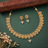 Gold-toned traditional necklace and matching dangle earrings with white pearl-like beads, arranged on a dark green background with a carved wooden prop and small dried flowers.