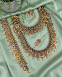 An ornate gold-toned traditional jewelry set laid out on mint green satin fabric, including a necklace, matching earrings, a bracelet, and a pendant. The pieces feature circular multicolor enamel motifs with red, yellow, blue, and green details, accented by small pearl-like beads.