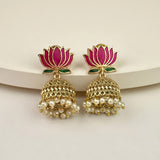 A pair of gold-plated Indian jhumka earrings with pink lotus flower studs, small green leaf accents, and dangling pearl bead clusters, displayed on a light beige surface.