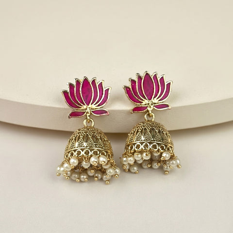 A pair of gold-toned Indian jhumka earrings with magenta-pink lotus flower studs and dangling pearl beads, displayed on a light beige surface.
