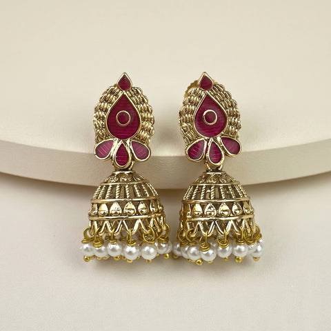 A pair of gold-plated Indian jhumka earrings with deep pink enamel inlays and dangling white pearl beads, displayed on a neutral cream background.