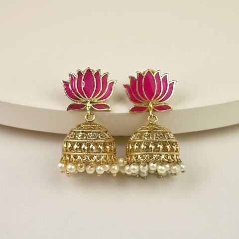 A pair of gold-plated Indian jhumka earrings with vibrant pink lotus flower tops and dangling white pearl chains, displayed on a neutral cream-colored surface.