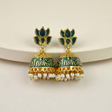 A pair of gold-plated Indian jhumka earrings with dark green enamel, intricate gold filigree, and dangling white faux pearls, displayed on a light beige curved surface.