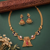 Gold-toned traditional necklace and matching earrings with red and blue stone accents, displayed on a dark green background with decorative dried flowers and a carved wooden prop.