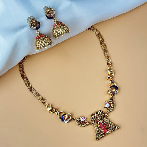 Gold necklace and earrings on a beige surface with a light blue background