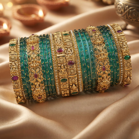 A stack of ornate Indian bangles, including turquoise green beaded bracelets and gold-plated filigree bangles with red and green stone accents, displayed on a beige satin fabric background.