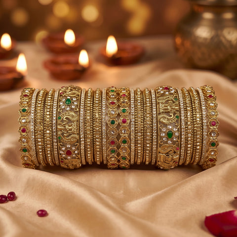 A stack of ornate gold bangles with intricate floral, geometric, and gemstone patterns, displayed on draped beige satin fabric with glowing diya candles in the background.