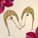 A pair of ornate gold filigree headbands decorated with small green and red gemstones, shown on a light beige background with pink flower petals in the corners.
