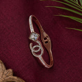 A rose gold bangle bracelet featuring a clear square crystal and a double-C logo design set with small crystals, displayed on a textured burgundy fabric background with decorative green leaves.
