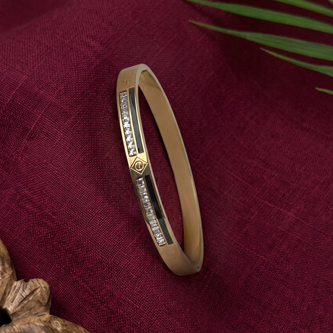 A gold-plated bangle bracelet with a central silver inlay set with small clear stones, displayed on a textured dark red fabric background.