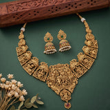 An ornate gold-toned jewelry set displayed on a dark green background, including a large filigree necklace, matching earrings, and small pearl-like bead accents. Decorative flowers and a carved wooden prop are placed around the set.