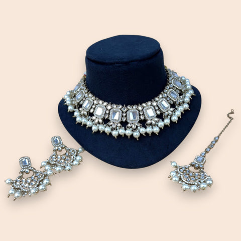 Jewelry set with necklace, earrings, and bracelet on a blue stand against a beige background