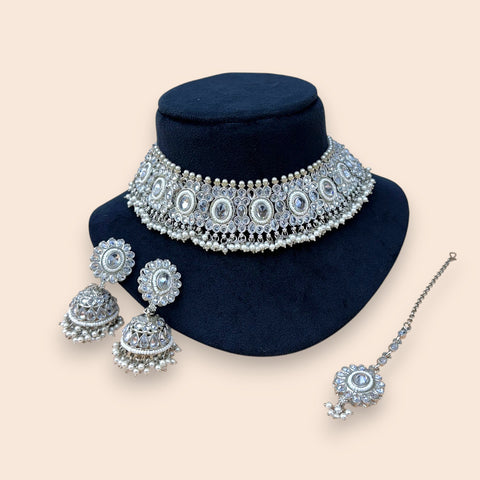 Silver jewelry set with necklace, earrings, and hairpin on a black stand against a beige background