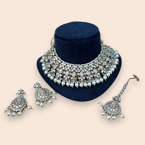 Jewelry set including a necklace, earrings, and a bracelet on a blue stand with a beige background.