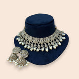 Ornate necklace with pearls and crystals on a navy stand against a beige background