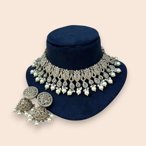 Ornate necklace with pearls and crystals on a navy stand against a beige background