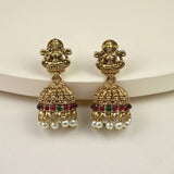 A pair of gold-plated Indian jhumka earrings featuring a detailed Ganesha motif on the studs, a decorative bell with red and green stones, and dangling white pearl beads, set against a neutral cream background.