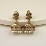 A pair of traditional Indian gold-plated jhumka earrings with Ganesha motifs, featuring red and green stone accents and dangling white pearl beads, displayed on a light beige background.