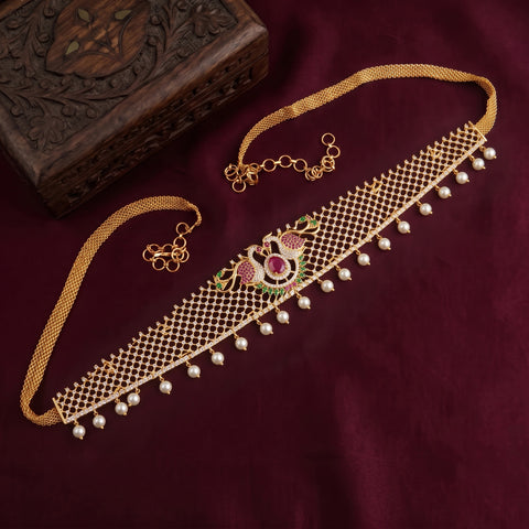 Gold-toned choker necklace with a central peacock motif in pink, green, and gold, accented with dangling white pearls, displayed on a deep burgundy fabric next to a carved wooden box.