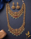 An ornate gold-toned traditional Indian jewelry set featuring a long necklace, a matching choker, and matching earrings, decorated with green and pink stones and white pearl-like beads, displayed on a dark navy background.