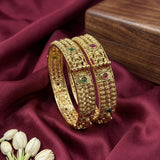 Gold bangles with gemstones on a maroon fabric background