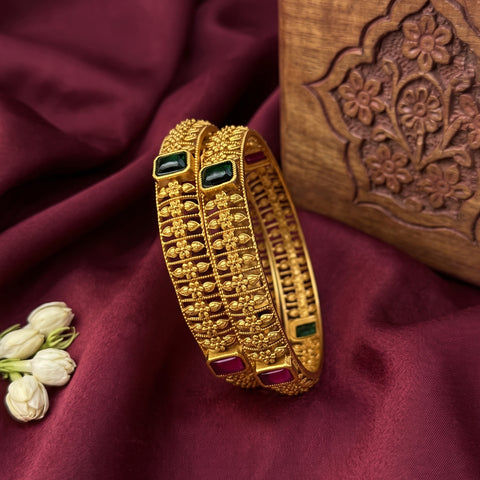 Gold bracelet with gemstones on a maroon fabric background