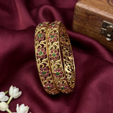 Gold bangles with gemstones on a maroon fabric background