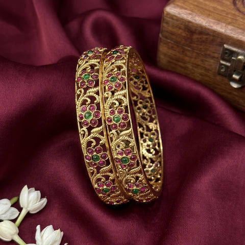 Gold bangles with gemstones on a maroon fabric background