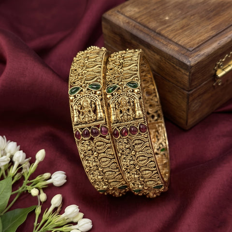 Gold bangles with gemstones on a maroon fabric background