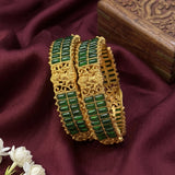 Gold bangles with green stones on a maroon fabric background