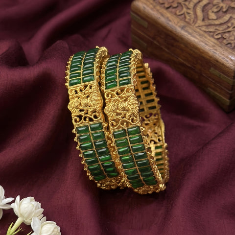 Gold bangles with green stones on a maroon fabric background