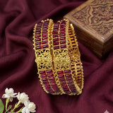 Gold bangles with red stones on a maroon fabric background