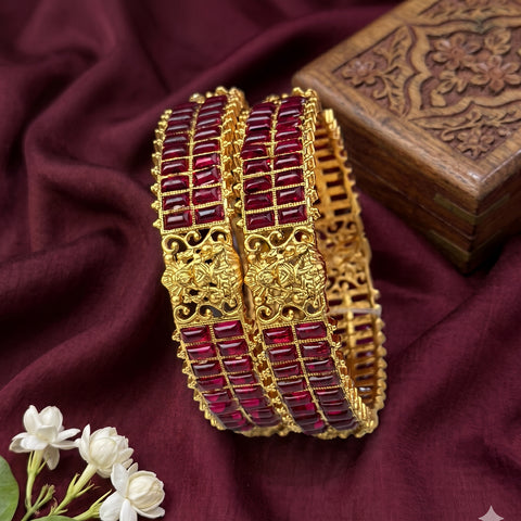 Gold bangles with red stones on a maroon fabric background