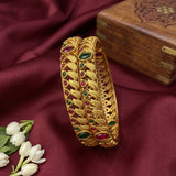 Gold bracelet with gemstones on a maroon fabric background