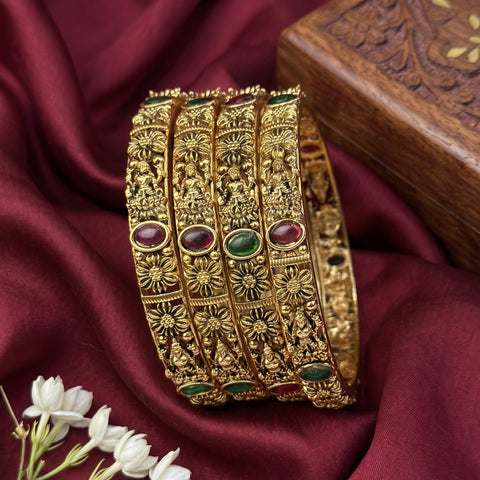 Gold bangles with gemstones on a maroon fabric background