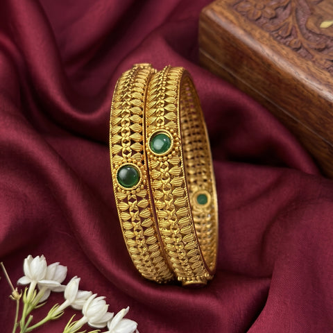 Gold bangles with green stones on a maroon fabric background