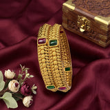 Gold bangles with gemstones on a maroon fabric background